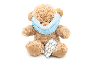 Teddy bear with protective medical mask with the pills isolated on a white background.