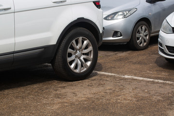 Fototapeta na wymiar Car on the Parking Spot. Alloy Wheel Closeup Photo. Lower Ground Level. Transportation and Automotive Theme.