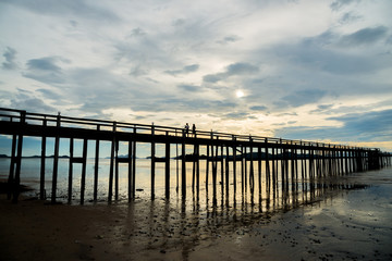 Silhouette view of the couple walking on the wooden bridge in sunset time at Ranong, Thailand.