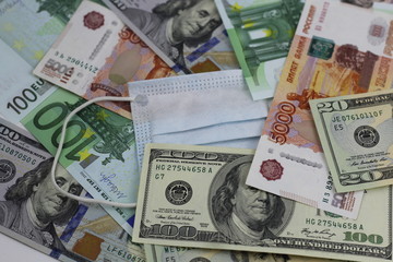 Obraz na płótnie Canvas Medical mask among the different denominations , dollars, euros and Russian rubles. Coronavirus as the cause of the global financial crisis in the spring of 2020