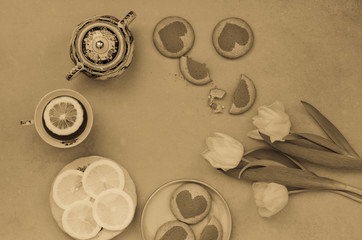 Flat lay a cup of tea , lemon slices, homemade cookies and white tulip flowers on a purple background. Top view