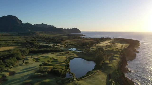 Low elevation aerial video of the southeast coast of Kauai with lava cliffs, green golf courses and mountain range. Poipu, Koloa, Kauai