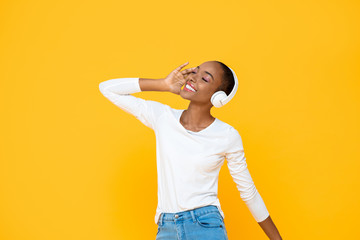 Happy African American woman enjoying listening to music on headphone isolated on colorful yellow background