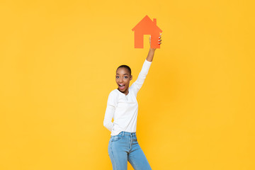 Confident smiling  African American woman holding up  house icon cut out in yellow isolated studio background