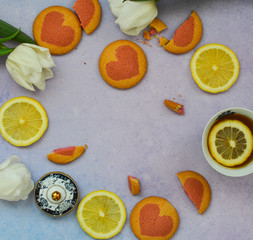 Flat lay a cup of tea , lemon slices, homemade cookies and white tulip flowers on a purple background. Top view