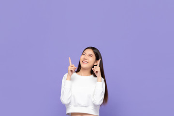 Portait of cute smiling young Asian woman pointing hands up and looking at blank space above in...