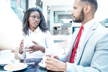 Obraz premium Diverse business colleagues chatting during coffee break. Business man and woman sitting in cafe, drinking coffee, talking and smiling. Coffee break concept