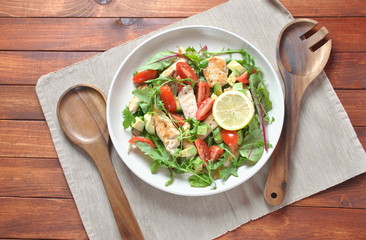 Chicken salad with avocado and cherry tomatoes, arugula and beet leaves. Healthy lunch bowl with vegetables and chicken on a wooden background. Healthy food concept