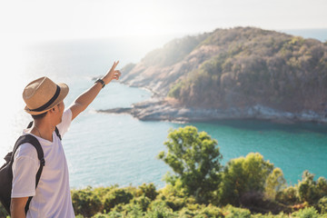 Man wearing hat holds his hand happy. Man asian tourist Look at mountains and the sea Before sunset.for activity lifestyle outdoors freedom or travel tourism inspiration backpacker tourist to covid 19