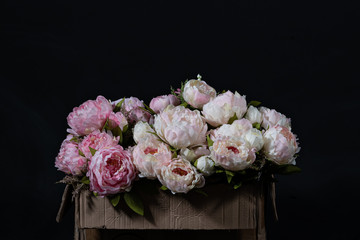 bouquet of pink and white peonies in carton box on black background.