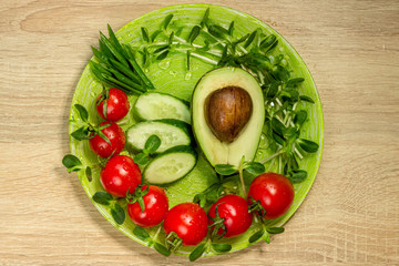 Homegrown sunflower micro green sprouts, cherry tomatoes, avocado, cucumber, green onion on the plate top view. Food ingredients on wooden table. Food photography. Health and growing concept.