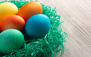 Colorful easter eggs in the green nest on the white wooden background. Happy easter concept.