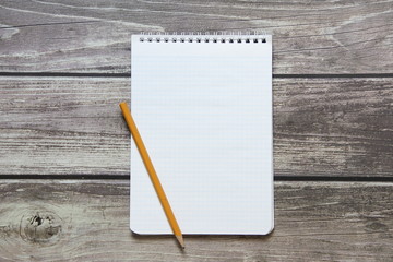 Notepad with a blank white sheet in a checker paper with simple graphite pencil lies on the background of wooden boards.