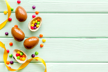 Easter background with chocolate eggs and dragees on green wooden background top-down frame copy space