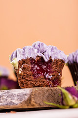 Chocolate cupcakes on a wooden table with flowers from the cremama, with fruit jam inside.