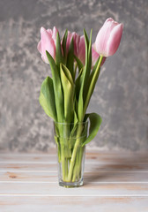 Beautiful delicate pink tulips in a glassy glass against a light background.