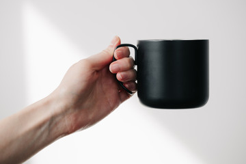 Black metal cup for tea and coffee in woman hand over white background