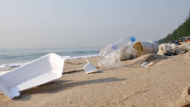 4K Garbage foam containers falling down on sand. Polluted beach in Asia, plastic bottles, bags, wastes on seashore. Plastic pollution crisis, environmental awareness concept.