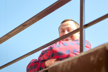 Obraz premium Man look down from above leaning on a metal railing. Brother and sister outdoors against a blue sky on a summer day