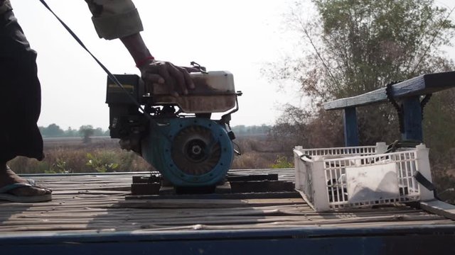 Khmer man on bamboo train pull starting old overhead valve engine with rope