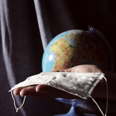 protective mask in hand on a background of blurry silhouette of the planet earth. preparing for a...