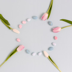 Wreath made of colorful easter eggs and flowers on a blue pastel background.