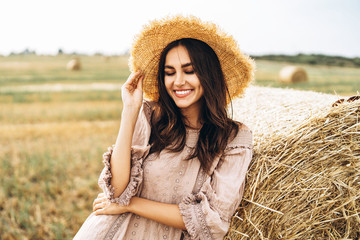 Closeup portrait of beautiful smiling woman with closed eyes. The brunette leaned on a bale of hay. A wheat field on the background