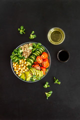 Healhty vegan lunch bowl. Avocado, quinoa, sweet potato, tomato, spinach and chickpeas vegetables salad om black table. Top view