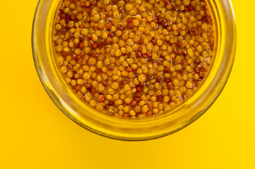 French mustard in a glass jar, shot on a yellow background. Background for seasoning and nutrition.