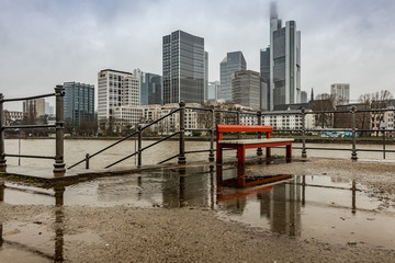 Spiegelung Bank in Regenpf&uuml;tze vor Frankfurter Skyline 