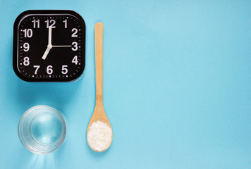 Fish collagen peptides powder and glass of water on blue background. alarm clock near wooden spoon with collagen.