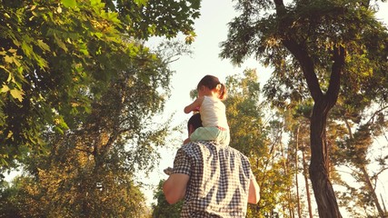 Fototapeta na wymiar Dad carries on shoulders of his beloved child, in park. Father walks with his daughter on his shoulders under trees. child with parents walks on day off. Happy family is relaxing in park.