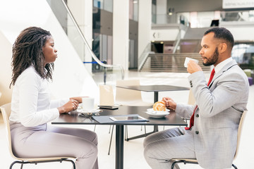 Fototapeta premium Diverse partners or colleagues meeting over cup of coffee. Side of business man and woman sitting at table in cafe, drinking coffee and talking. Business meeting or coffee hour concept