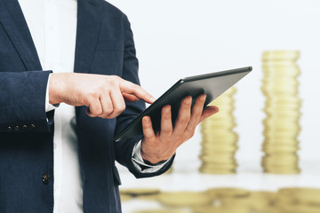 Man presses on the screen of a digital tablet on the background of stacks of gold coins, close up. Online Investment concept