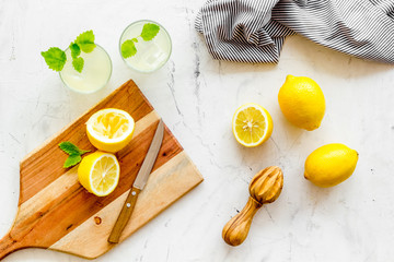 Homemade lemonade in glasses near juicer and cut lemons on white background top-down