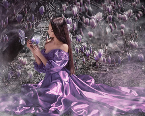 Portrait of amazing cute young woman with dark brown long hair in long purple dress sitting under...