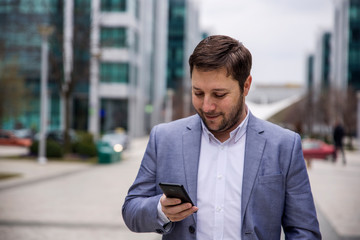 Businessman using smartphone Outdoors in front of Office Building. Texting, Sms, Internet Surfing, App, Communication. Corporate Business Concept