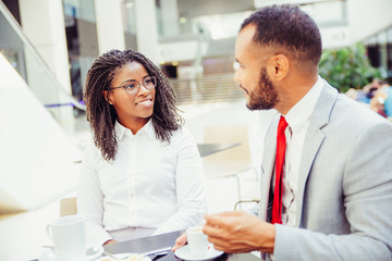 Friendly office colleagues enjoying coffee break together. Business man and woman sitting in cafe, drinking coffee, talking and smiling. Coffee hour concept