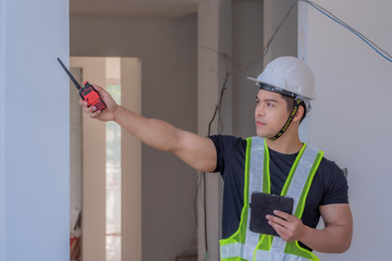 Strong foreman wearing a white helmet, holding a radio communication and a tablet on the...