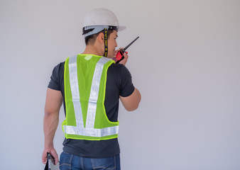 Strong foreman wearing a white helmet, holding a radio communication and a tablet on the...