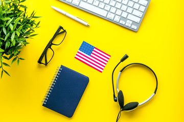 Learn English online. Concept with American - USA - flag, headset and keyboard on yellow background top-down