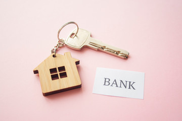Wooden house toy and silver key on bright pink background with phrase quote Bank. Mortgage, house buy sell, investment, rent, realtor concept