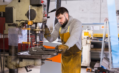 Workman drilling metal parts on stationary machine