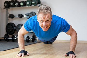Mature smiling man doing push-ups in a gym