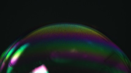 Rainbow soap bubble on a dark background. Close-up of colorful surface