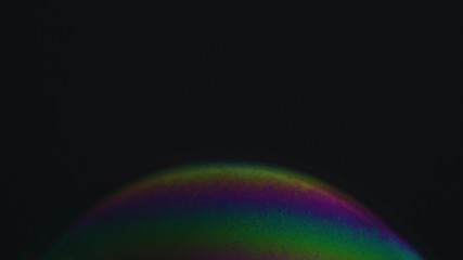 Rainbow soap bubble on a dark background. Close-up of colorful surface