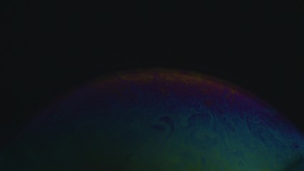Rainbow soap bubble on a dark background. Close-up of colorful surface