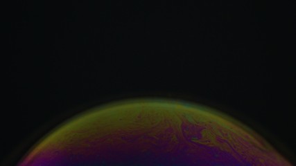 Rainbow soap bubble on a dark background. Close-up of colorful surface