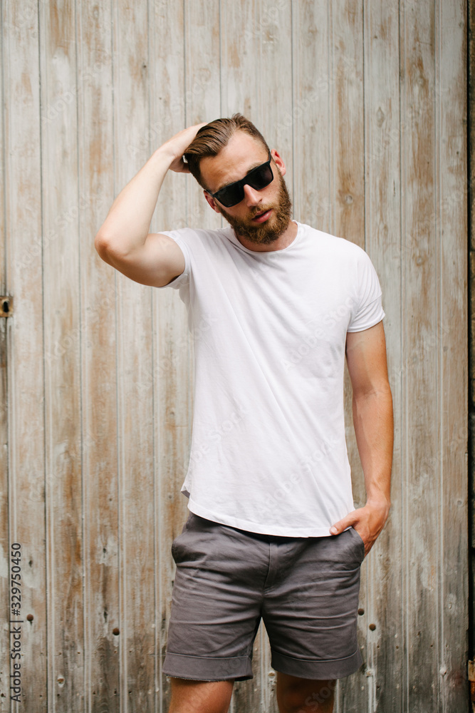 Wall mural hipster handsome male model with beard wearing white blank t-shirt and a baseball cap with space for