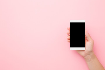 Young woman hand holding smartphone with black screen on light pink table background. Pastel color. Empty place for text. Closeup. Top down view.
